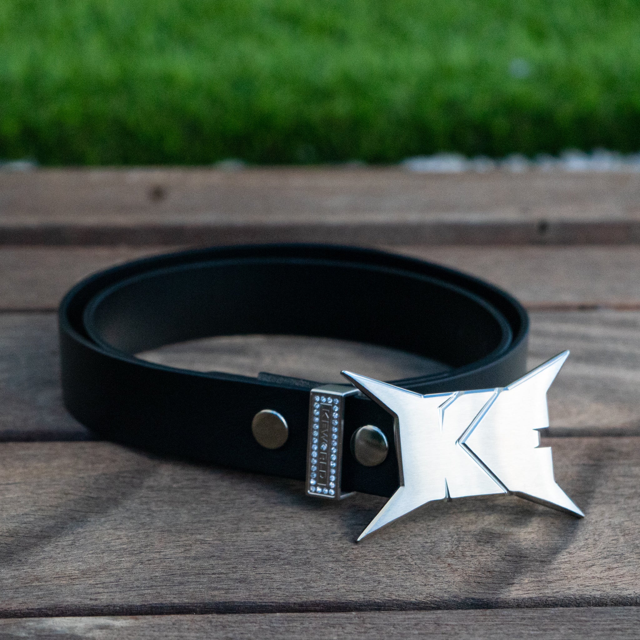 Black belt with a silver and black star-shaped buckle on a wooden surface with grass in the background