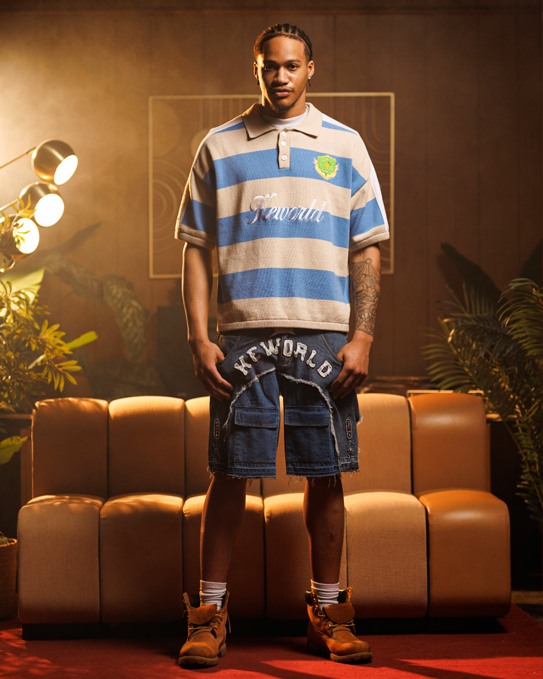 Man wearing a striped polo shirt and cargo shorts in a room with a couch and plants.