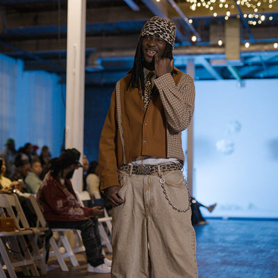 Person in a stylish outfit with a brown jacket and beige pants standing indoors.