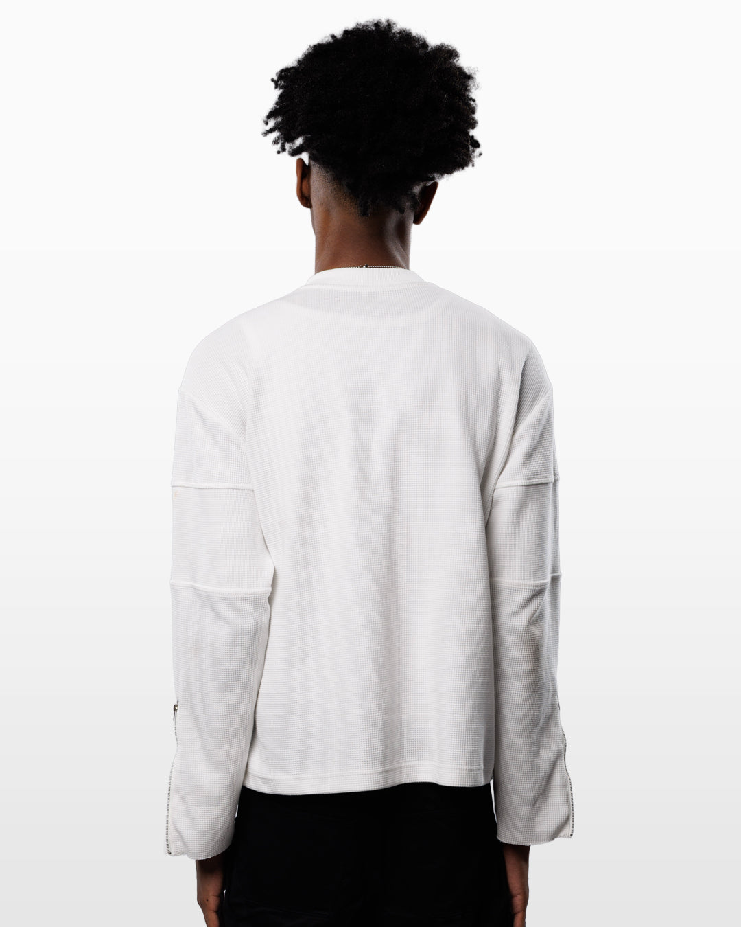 A person shown from the back wearing a white long-sleeve top with unique seam detailing on the sleeves, paired with black bottoms, against a plain white background.