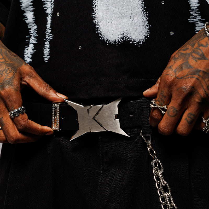 Person wearing a black outfit with a unique belt buckle and chain, holding the waist.